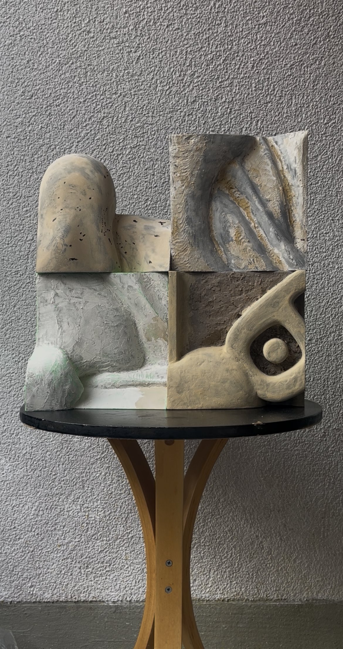 Study I: a stacked sculptural composition of four carved, hand-painted blocks — a rounded hump form, a grain-textured slab, a smooth curved panel, and a hooked, eye-like element — in a muted grey and bone palette.